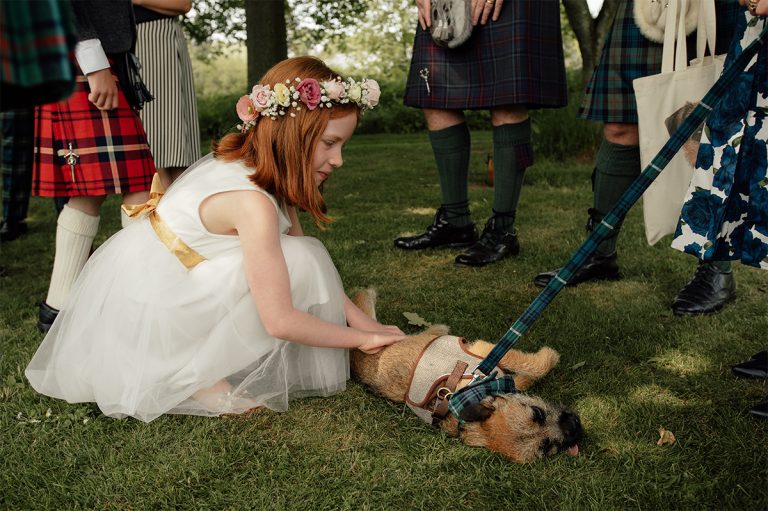 Flower girls playing with a dog at a wedding venue in Scotland.